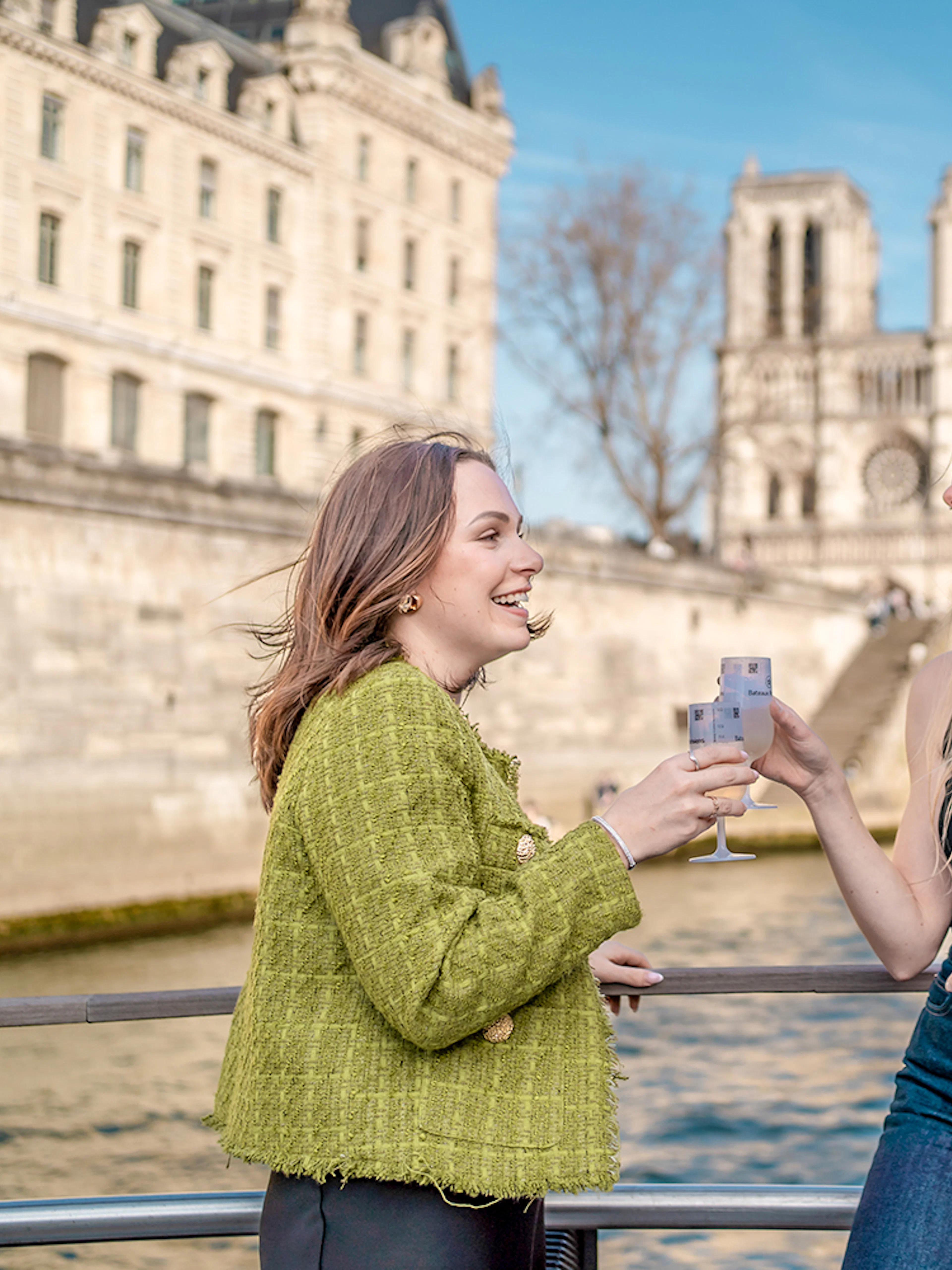 People enjoying champagne on a Seine River cruise with Notre-Dame Cathedral in the background.