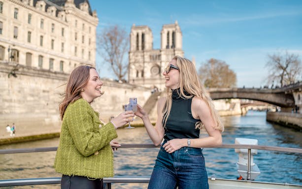 People enjoying champagne on a Seine River cruise with Notre-Dame Cathedral in the background.