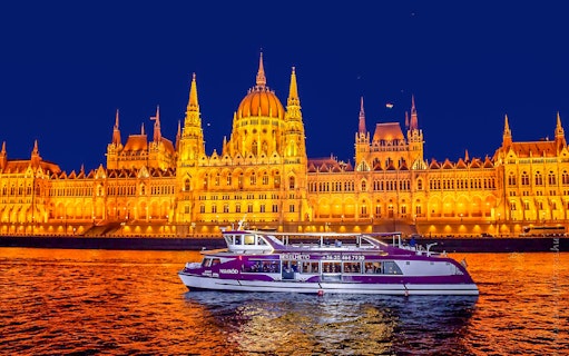 Budapest Parliament lit up at night with a cruise boat on the Danube River.