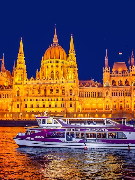 Budapest Parliament lit up at night with a cruise boat on the Danube River.