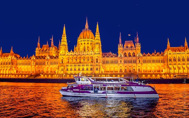 Budapest Parliament lit up at night with a cruise boat on the Danube River.