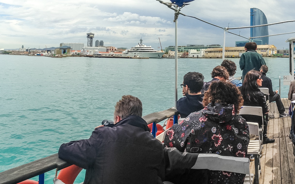 Tourists on Las Golondrinas boat viewing Barcelona skyline with W Hotel in background.