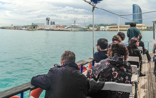 Tourists on Las Golondrinas boat viewing Barcelona skyline with W Hotel in background.