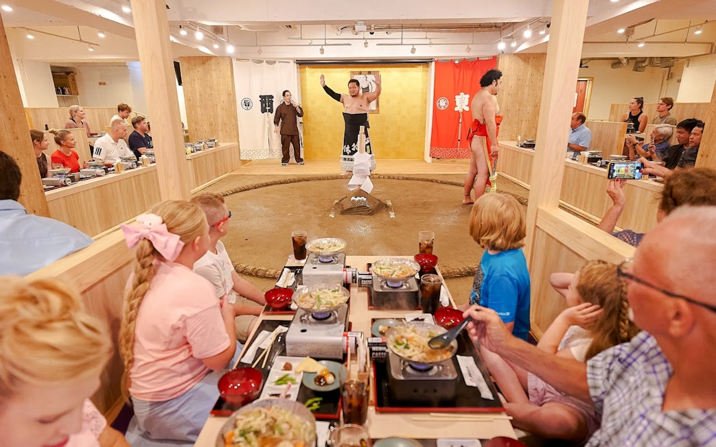 Family watching sumo show with retired wrestler at Ryogoku, enjoying chanko-nabe and mochi.