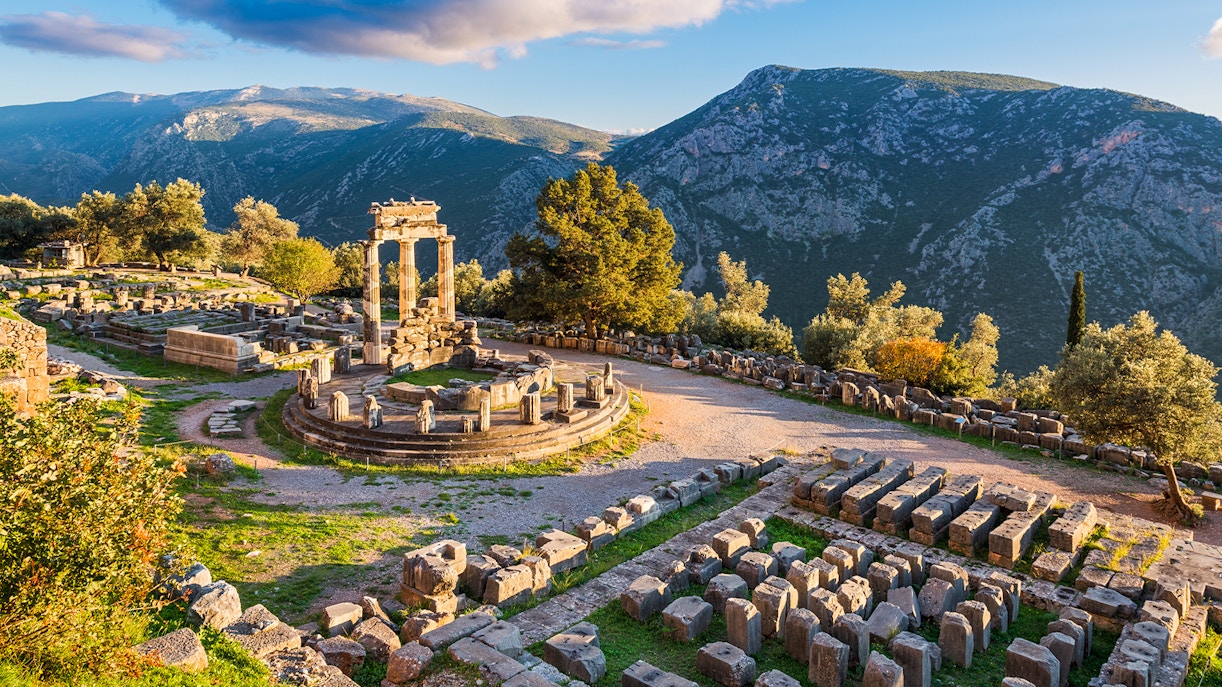 Temple of Athena Pronaia ruins with mountain backdrop in Delphi, Greece.