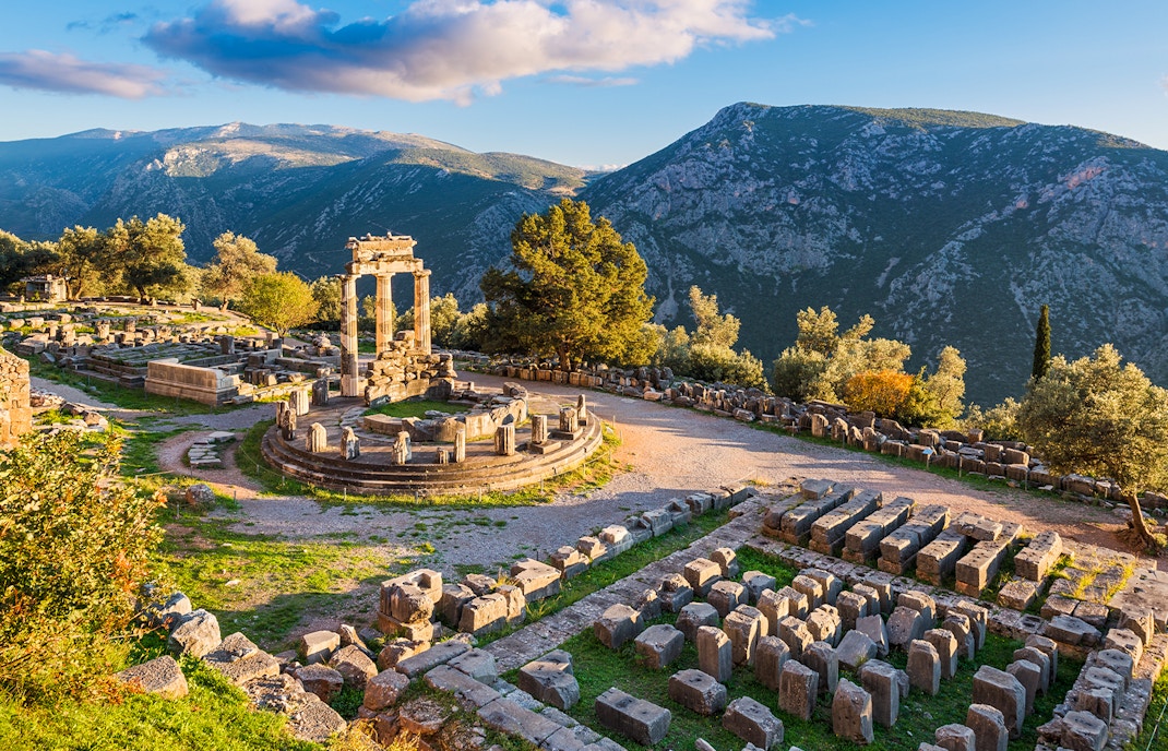 Temple of Athena Pronaia ruins with mountain backdrop in Delphi, Greece.