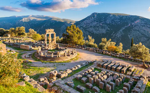 Temple of Athena Pronaia ruins with mountain backdrop in Delphi, Greece.
