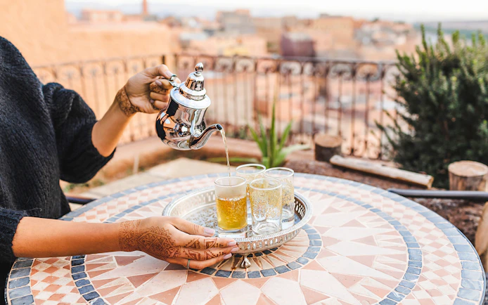 Pouring mint tea into glasses on a mosaic table in Jema el Fna, Marrakesh.
