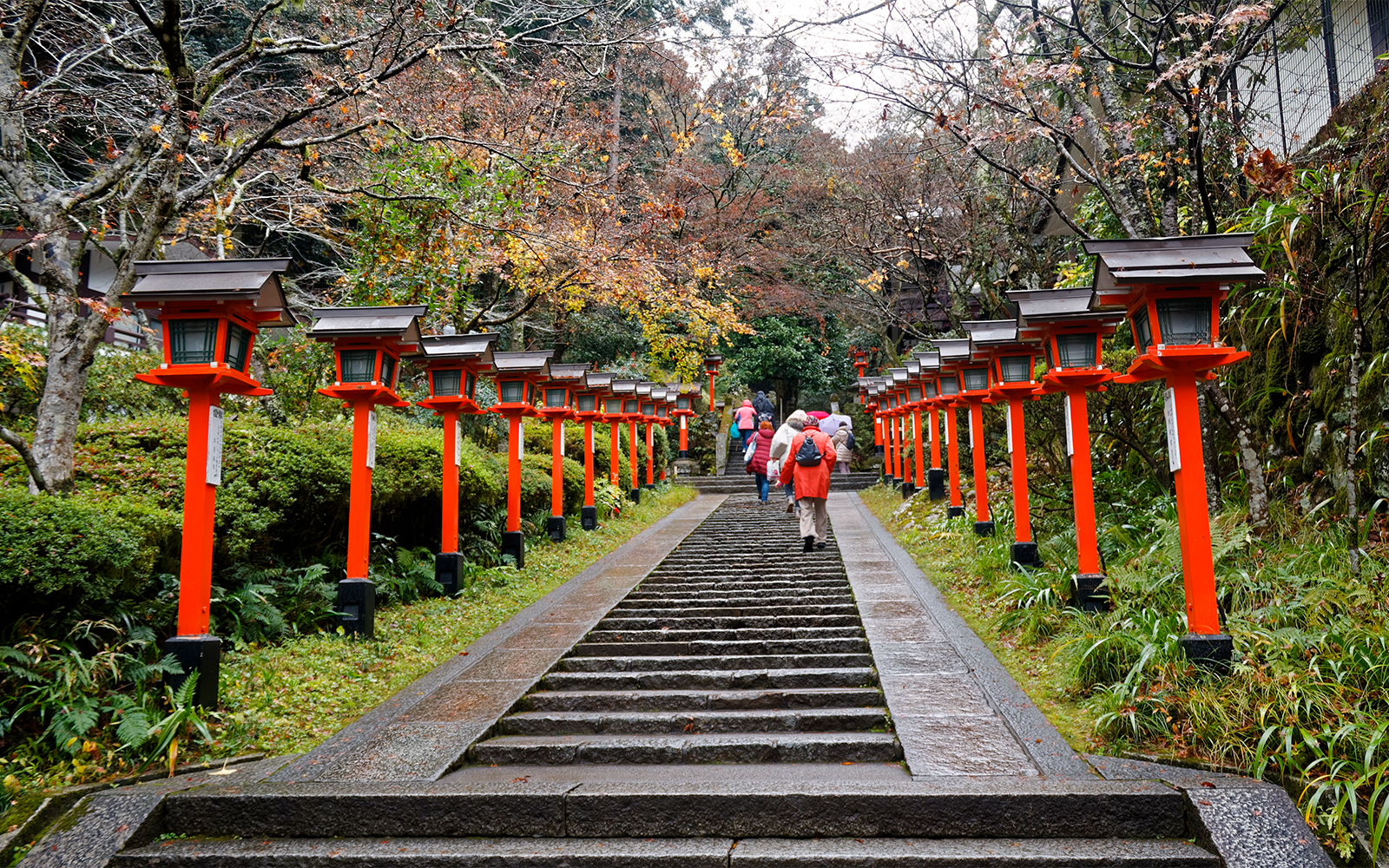 Steps lined with red lanterns leading to Kinkaku-ji temple, people walking up.