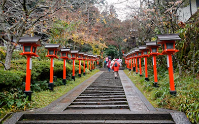 Steps lined with red lanterns leading to Kinkaku-ji temple, people walking up.
