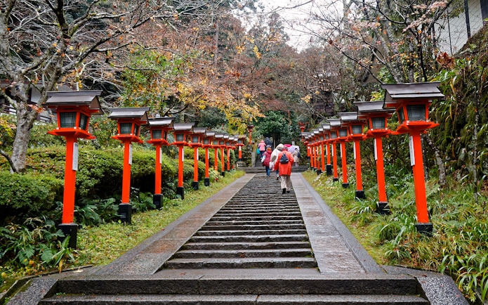 Steps lined with red lanterns leading to Kinkaku-ji temple, people walking up.