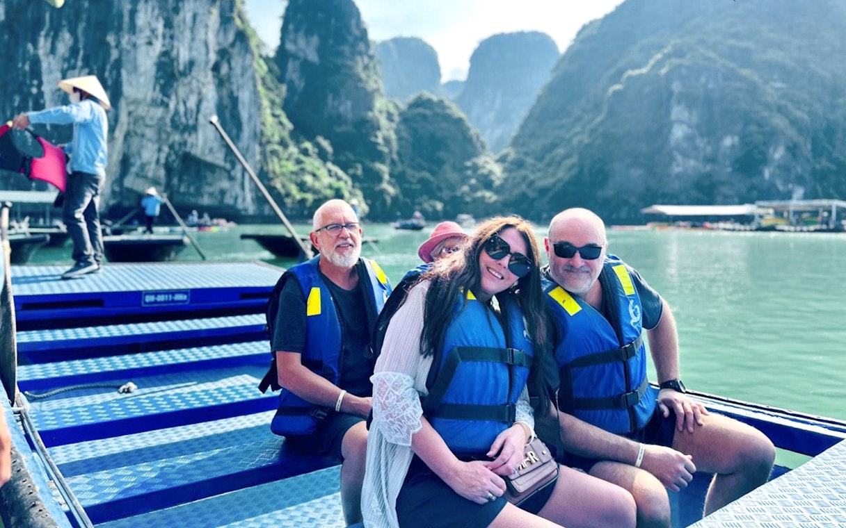 Tourists in life jackets on a boat in Ha Long Bay with limestone cliffs in the background.