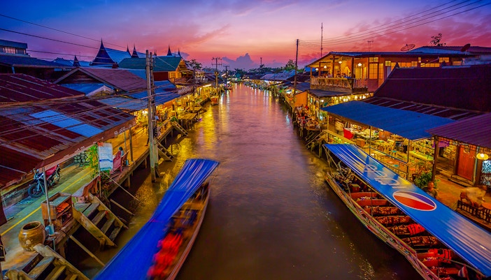 Amphawa canal bustling with boats and vendors at twilight in a vibrant village setting.