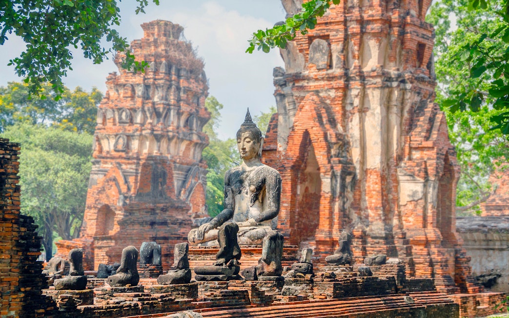 Ancient Buddha statue at Ayutthaya Historical Park, Thailand, with brick ruins in the background.