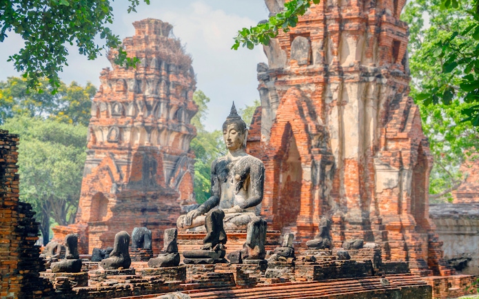 Ancient Buddha statue at Ayutthaya Historical Park, Thailand, with brick ruins in the background.
