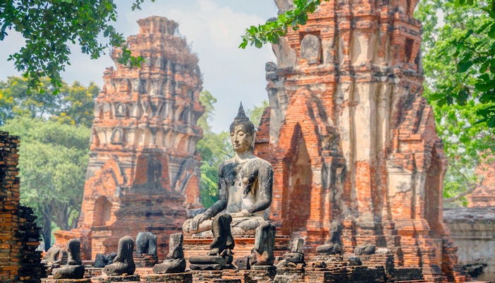Ancient Buddha statue at Ayutthaya Historical Park, Thailand, with brick ruins in the background.