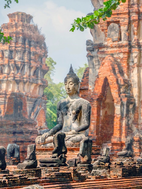 Ancient Buddha statue at Ayutthaya Historical Park, Thailand, with brick ruins in the background.