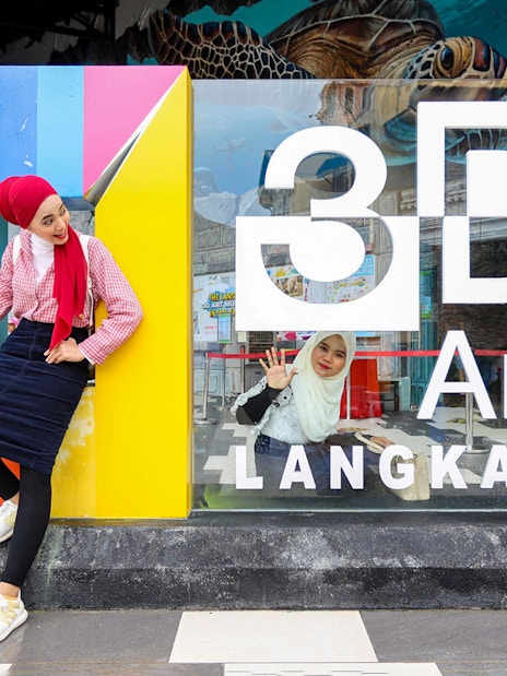 Women posing at 3D Art Langkawi entrance.