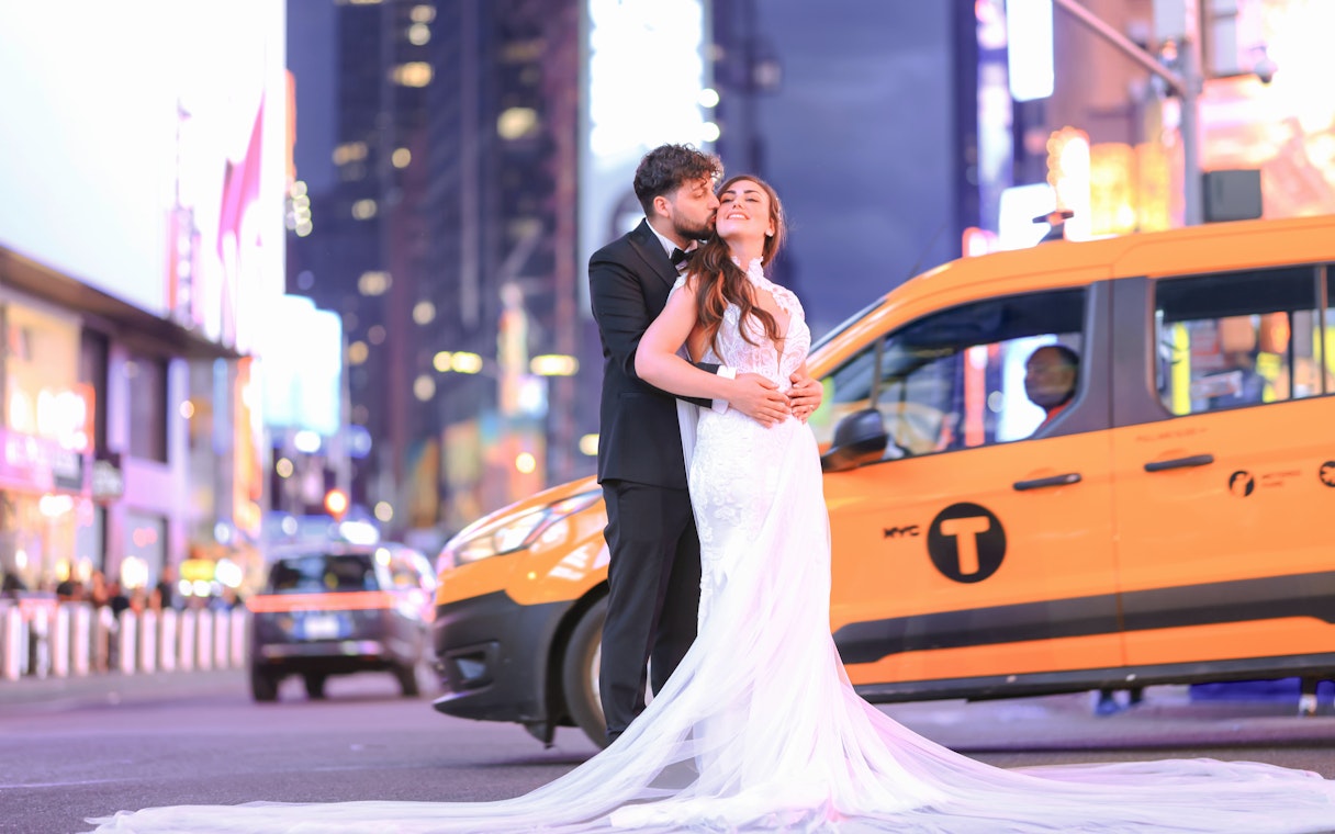 Couple embracing in Times Square, NYC with yellow taxi in background.