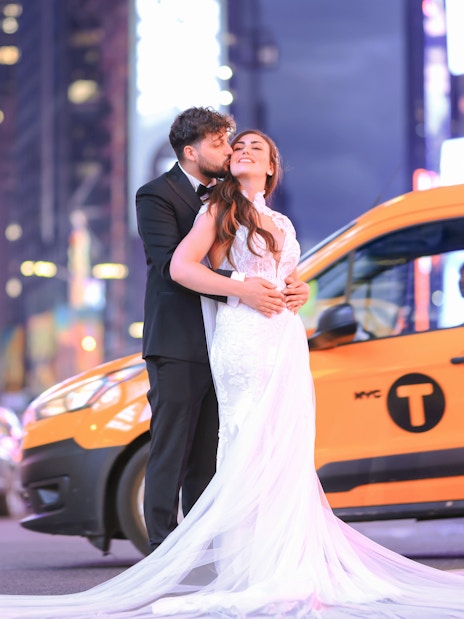 Couple embracing in Times Square, NYC with yellow taxi in background.