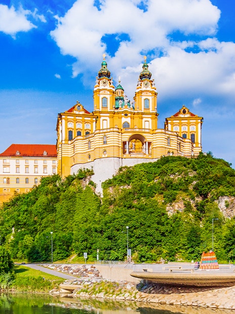 Melk Abbey exterior with baroque architecture in Vienna, surrounded by lush greenery.