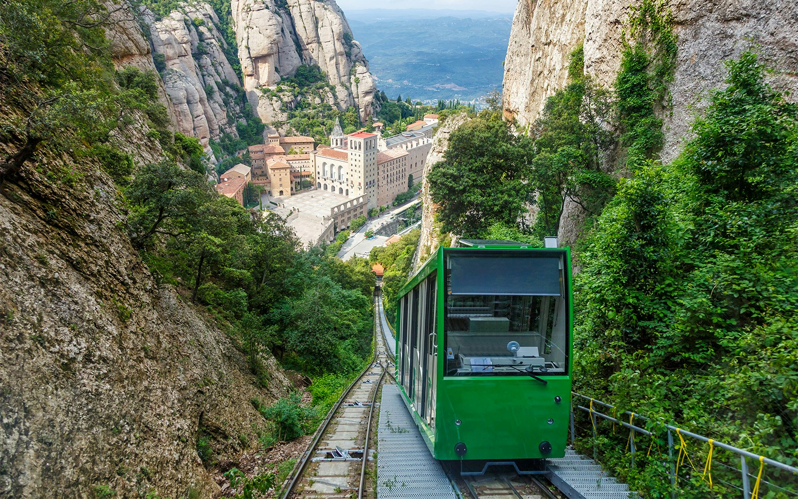 Cogwheel train ascending to Montserrat Monastery, surrounded by rocky cliffs and lush greenery.