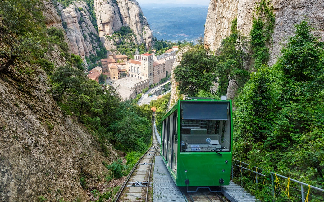 Cogwheel train ascending to Montserrat Monastery, surrounded by rocky cliffs and lush greenery.