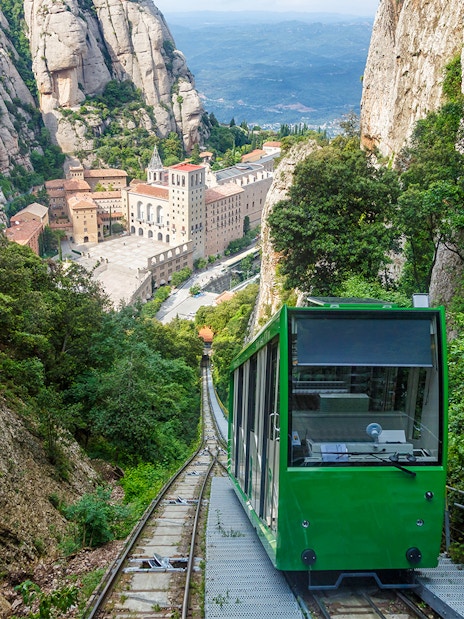Cogwheel train ascending to Montserrat Monastery, surrounded by rocky cliffs and lush greenery.