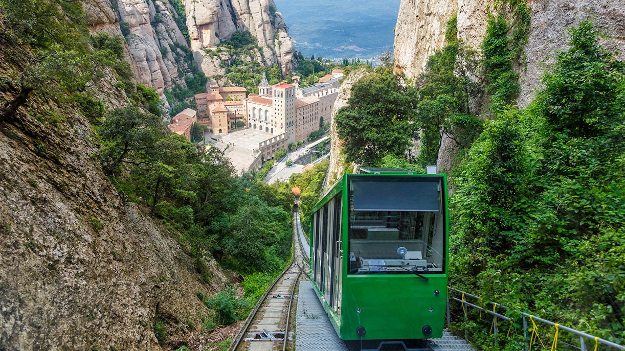 Cogwheel train ascending to Montserrat Monastery, surrounded by rocky cliffs and lush greenery.