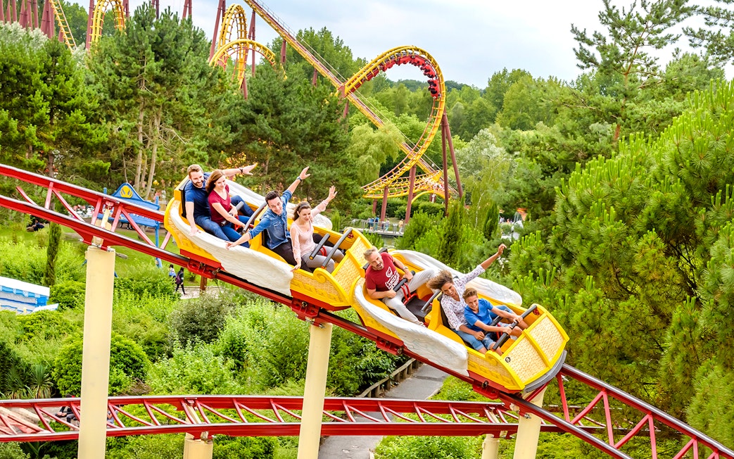 Visitors enjoying a roller coaster ride at Astérix Park, surrounded by lush greenery.