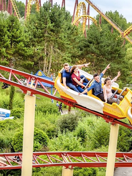 Visitors enjoying a roller coaster ride at Astérix Park, surrounded by lush greenery.