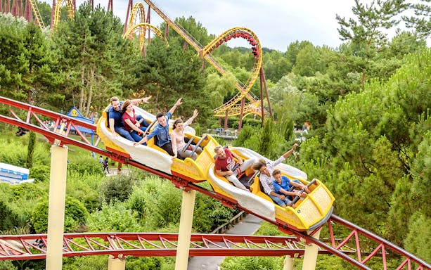 Visitors enjoying a roller coaster ride at Astérix Park, surrounded by lush greenery.
