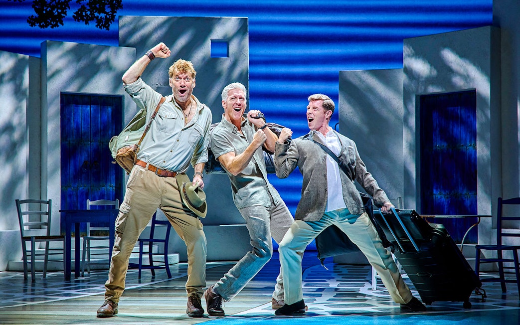 Three actors performing energetically on stage in a Mamma Mia production.