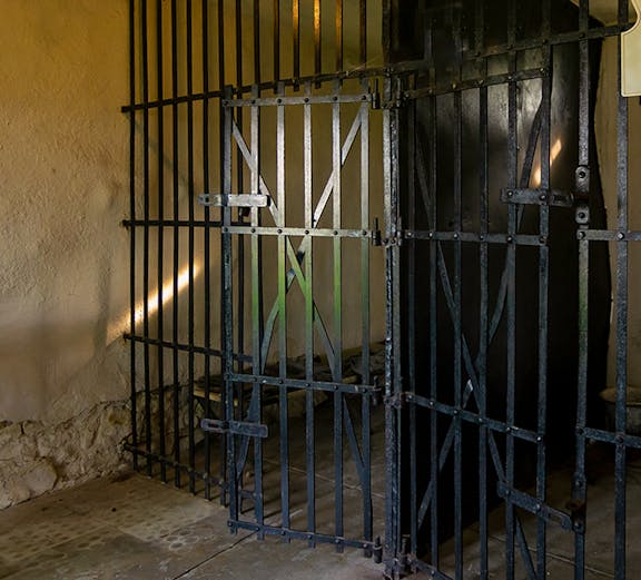Open cell door at Old Jail Museum with iron bars and dim lighting.