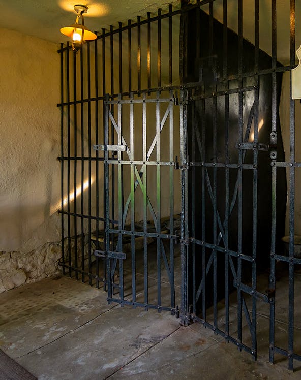 Open cell door at Old Jail Museum with iron bars and dim lighting.