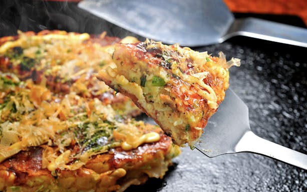Okonomiyaki being served on a spatula during a Tokyo street food tour in Shibuya.