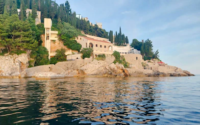 Dubrovnik coastline view from the sea, featuring historic stone buildings and lush greenery.