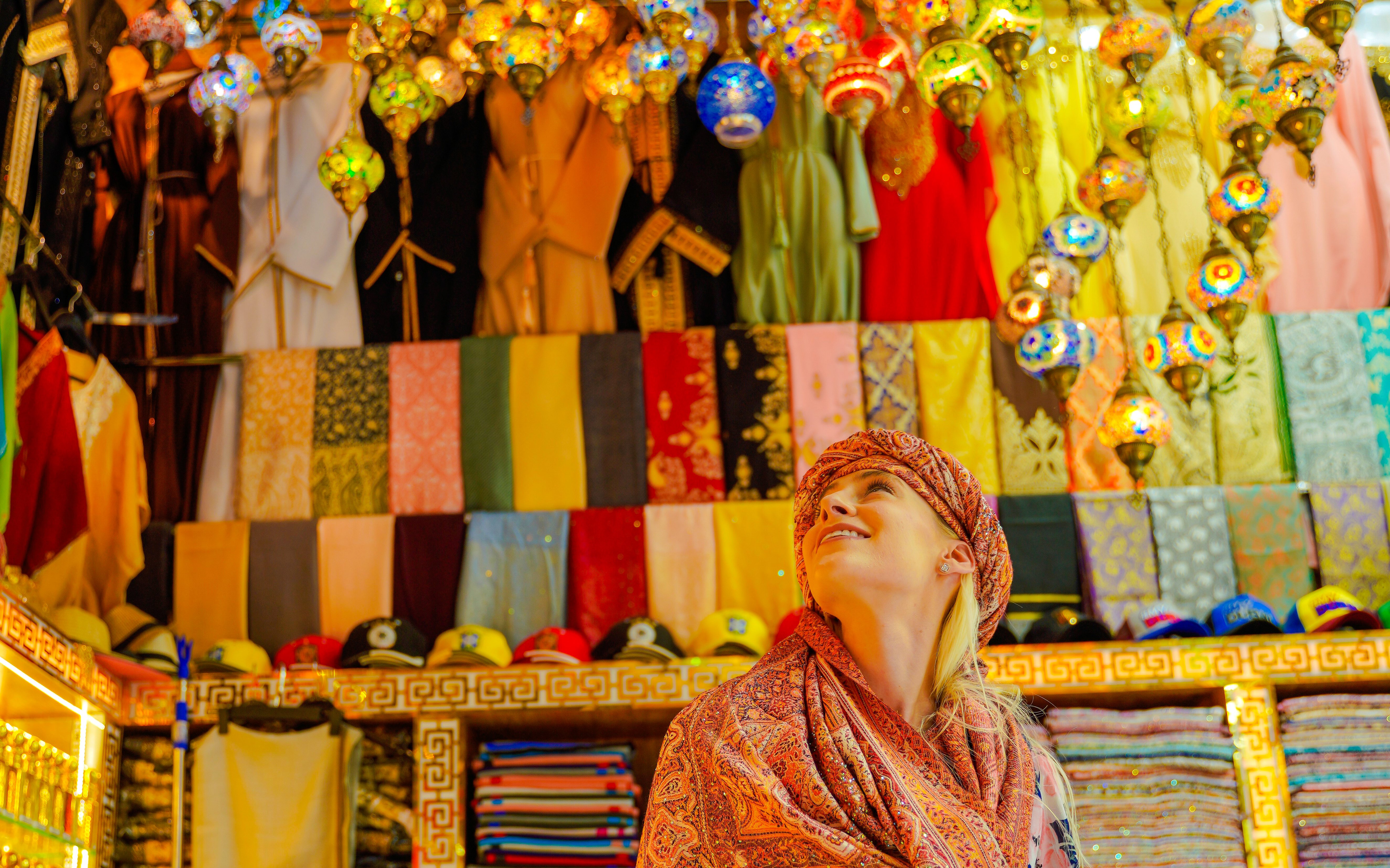 Visitor admiring colorful textiles and lanterns in a vibrant local market.