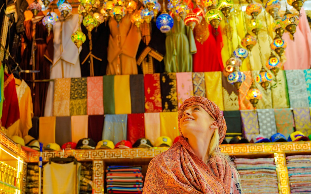 Visitor admiring colorful textiles and lanterns in a vibrant local market.