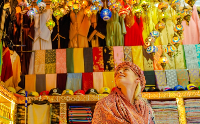 Visitor admiring colorful textiles and lanterns in a vibrant local market.