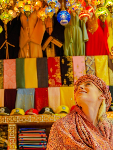 Visitor admiring colorful textiles and lanterns in a vibrant local market.