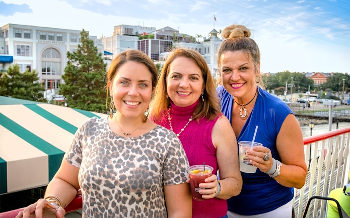 Group enjoying drinks on the Riverboat City of New Orleans with cityscape in background.