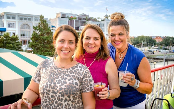 Group enjoying drinks on the Riverboat City of New Orleans with cityscape in background.