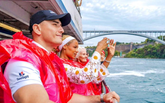 Tourists in red ponchos on a boat cruise at Niagara Falls, Canada, with a bridge in the background.