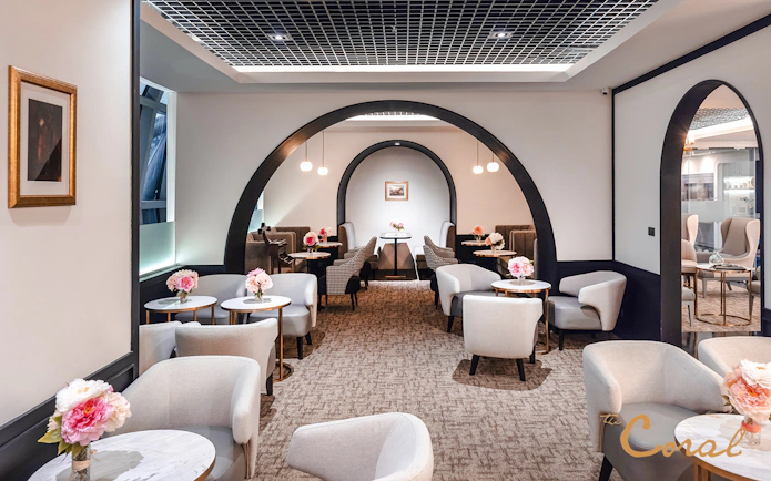 Coral First Class Lounge seating area with tables and flowers, Bangkok airport, Thailand.