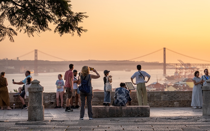 Visitors capturing sunset views from St George's Castle with Lisbon's bridge in the background.