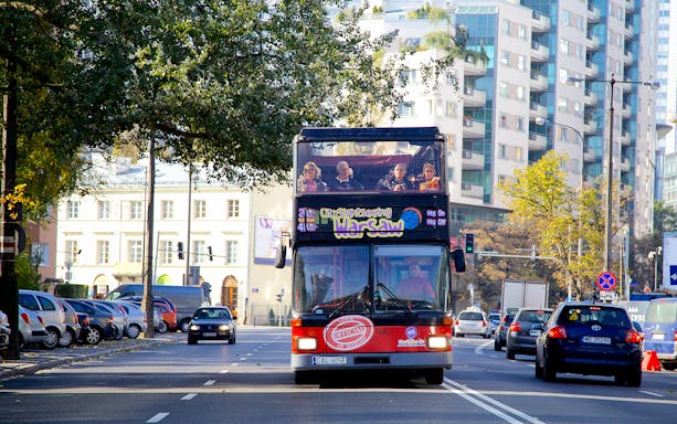 Hop-on hop-off bus on Warsaw street with tourists on upper deck.