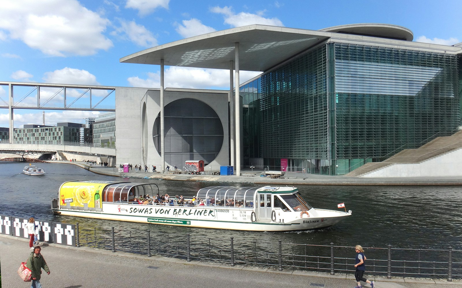 Sightseeing boat on Spree River, Berlin Mitte, with cityscape in background.