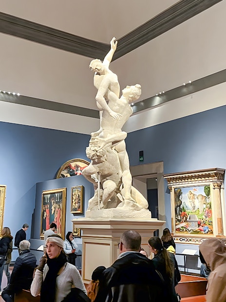 Sculpture of the Rape of Sabine Women at Accademia Gallery, Florence, surrounded by visitors.