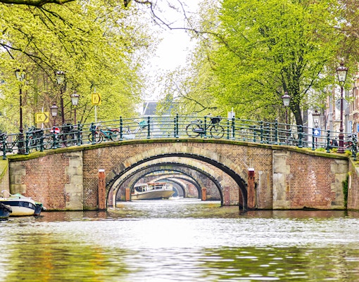 Canal view of seven bridges in Amsterdam with bicycles and trees lining the path.